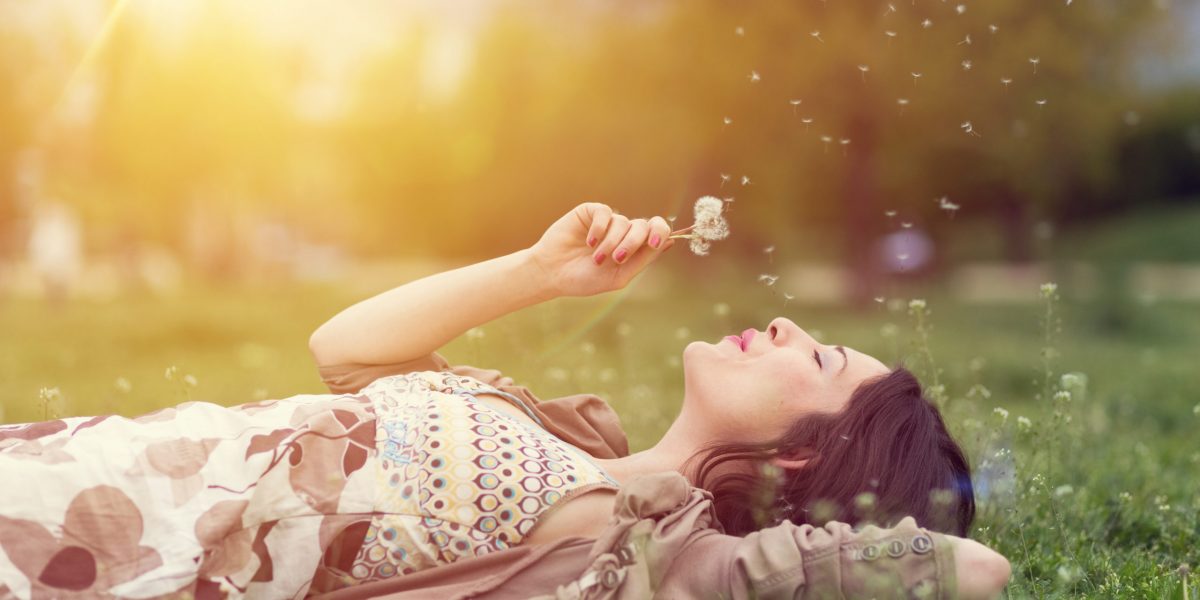 Young woman lying down in the grass and blowing dandelion